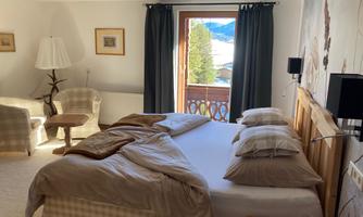 A cozy bedroom with a large bed and a beautiful view of the mountains through the window. The decor is modern and inviting, with comfortable armchairs and soft colors.