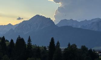 An impressive mountain landscape with majestic peaks and a dramatic sky. In the foreground, a green meadow stretches out.