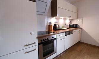 A modern kitchen with white cabinets and a wooden countertop. It includes cooking appliances, a kettle, and a microwave.