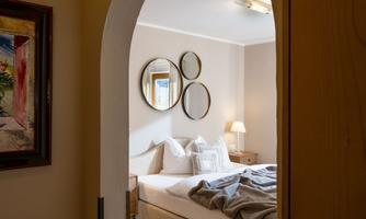 An inviting bedroom with a large bed and several mirrors on the wall. Through a semi-open archway, the cozy atmosphere is clearly visible.