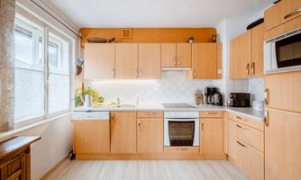 A bright kitchen with wooden cabinets and modern appliances. There are large windows that let in plenty of light.