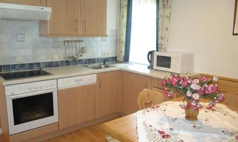 A modern kitchen with wooden cabinets and a bright countertop. A vase with flowers is on the table, and next to it is a microwave.