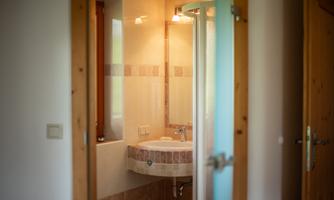 A modern bathroom with a sink and a shower. It has a large window that lets in daylight.