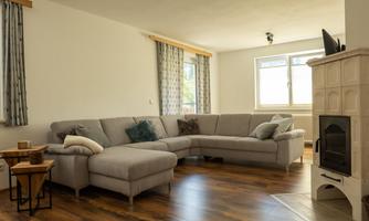 A bright living room with a large gray corner sofa. Next to it is a small wooden table and a fireplace in the corner.