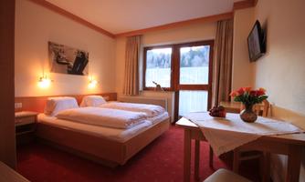A cozy hotel room with two beds and a table. Large windows offer a view of the landscape and fresh flowers on the table.