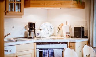 A cozy kitchen with light wooden furniture and modern appliances. On the countertop, there is a coffee machine and dishes.
