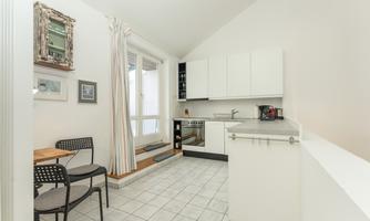A bright and modern kitchen with white cabinets and a small seating area. Large windows provide plenty of daylight.