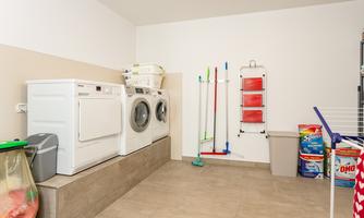A modern laundry room with a washing machine and a dryer. Cleaning supplies and detergents are neatly arranged.