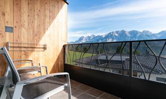 A cozy balcony with two chairs and a view of the mountains. The surroundings are quiet and sunny.