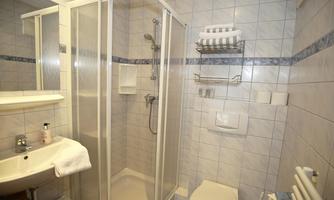 A modern bathroom with shower, sink, and toilet. The walls are tiled with light tiles.