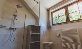 A modern bathroom with a walk-in shower and a window. The walls are light and the fixtures are functional.