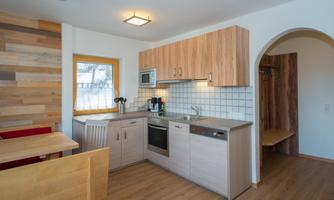 A modern kitchen with wooden cabinets and a bright, inviting atmosphere. The dining area is simply and functionally furnished.