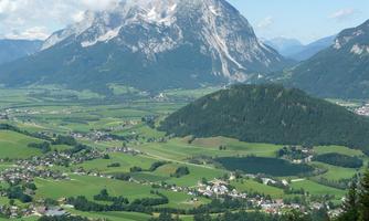 An impressive mountain landscape with green meadows and small villages. Majestic mountains rise in the background under a clear sky.