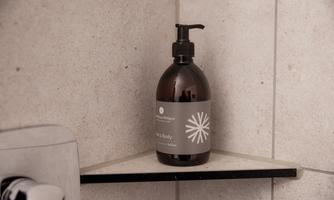 An elegant shampoo bottle on a shower shelf. The bottle has a simple design and is placed in a modern bathroom.