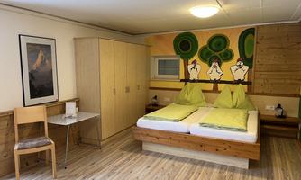 A cozy room with wooden furniture and light bedspreads. On the wall, there is a colorful painting with green trees and figures.