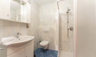 A modern bathroom with a shower, sink, and toilet. The walls are tiled in light colors, and the floor is blue.