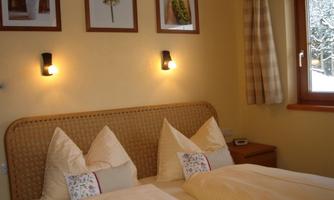A cozy bedroom with two beds and decorative pillows. The walls are painted light and adorned with pictures.