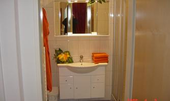 A simple bathroom with a sink, a mirror, and a shower. Orange towels and a plant provide a colorful accent.