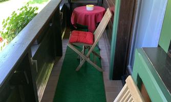 A small balcony with two wooden chairs and a round table. The floor is covered with green carpet and there is a view of the outdoors.