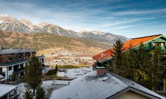 A picturesque mountain landscape with snow-capped peaks and a serene valley. In the foreground, there are houses and trees that frame the natural beauty.