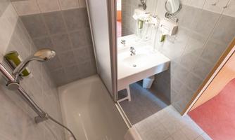 A modern bathroom with a shower and a bathtub. The wash area is well-equipped and brightly designed.