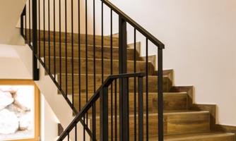 A modern staircase with wooden steps and a black railing. Some small shelves are mounted on the wall, softly illuminated.