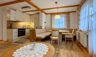 A modern living room with an open kitchen and a dining table. The wooden ceiling and the table give the room a cozy atmosphere.