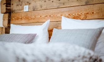 A cozy bedroom with a wood panel and several cushions on the bed. The atmosphere is warm and inviting.