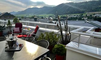 A cozy terrace with a beautiful view of the mountains. There is a dining table, chairs, and decorative plants.