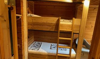 A cozy room with a loft bed and an additional bed. The walls are made of wood, and there is a warm, inviting look.