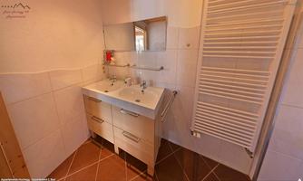 A modern bathroom with a double sink and a large mirror. The walls are light tiled and the floor has an elegant tile look.