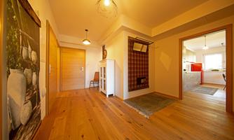 An inviting hallway with wooden flooring and warm light. Modern decorations hang on the wall and the access to a bright kitchen is visible.
