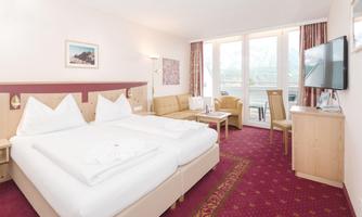 A cozy hotel room with a double bed and a sofa. Large windows provide plenty of daylight and a view outside.