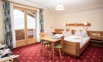 A cozy bedroom with a double bed and a table with chairs. Large windows let in plenty of natural light and offer a view of the surroundings.