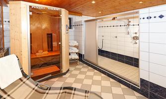 A relaxing sauna area with a wooden sauna and a shower. The floor is tiled and towels are nearby.