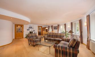 A bright living room with checkered sofas and a glass table. Large windows let in plenty of light and there are plants for decoration.