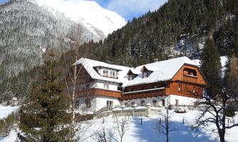 A picturesque wooden house amidst a wintry landscape. The snow covers the surroundings, and in the background, majestic mountains rise.