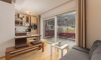 A modern apartment with an open kitchen and a cozy living room. Large windows offer a view of the surrounding landscape.