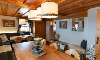 A cozy dining area with a large wooden table and modern lamps. The walls are covered with wood and there is a pleasant, inviting atmosphere.