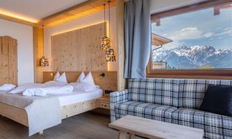A cozy bedroom with a wooden bed and a seating area. An impressive mountain landscape can be seen through the window.