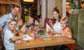 A family is sitting at a table in a restaurant enjoying their meal. They are smiling and have drinks in front of them.