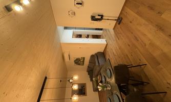 A modern living room with a cozy sofa and a dining table. The room has wooden flooring and warm lighting accents.