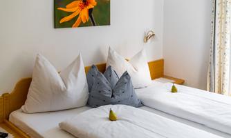 A bedroom with two single beds and decorative pillows. A picture of a yellow flower hangs on the wall.