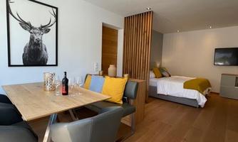 A modern room with a dining table and chairs. In the background, there is a bed and a wall with wooden elements.