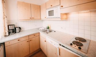 A modern kitchen with wooden cabinets and a bright countertop. It is equipped with a stove, a microwave, and a coffee machine.