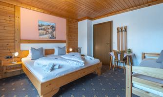 A cozy room with wooden ceilings and a double bed. There is a small seating area and a decorative picture on the wall.