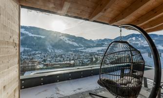A cozy terrace with a hanging basket chair and a view of snow-capped mountains. The sun is shining and illuminating the picturesque landscape.