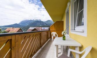 A balcony with a table and chairs, surrounded by a beautiful mountain landscape. In the background, majestic mountains can be seen under a cloudy sky.