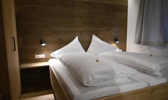 A cozy bedroom with a double bed and large pillows. The walls are made of wood and there is soft lighting.