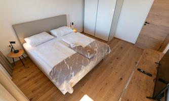 A modern bedroom with a double bed and light wooden floor. The walls are kept neutral and there is an elegant wardrobe.